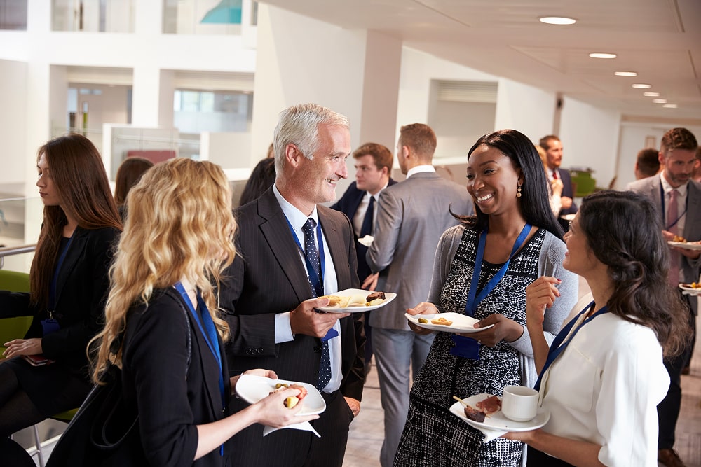 A group of diverse professionals networking at a business event, smiling and talking during a lunch break.