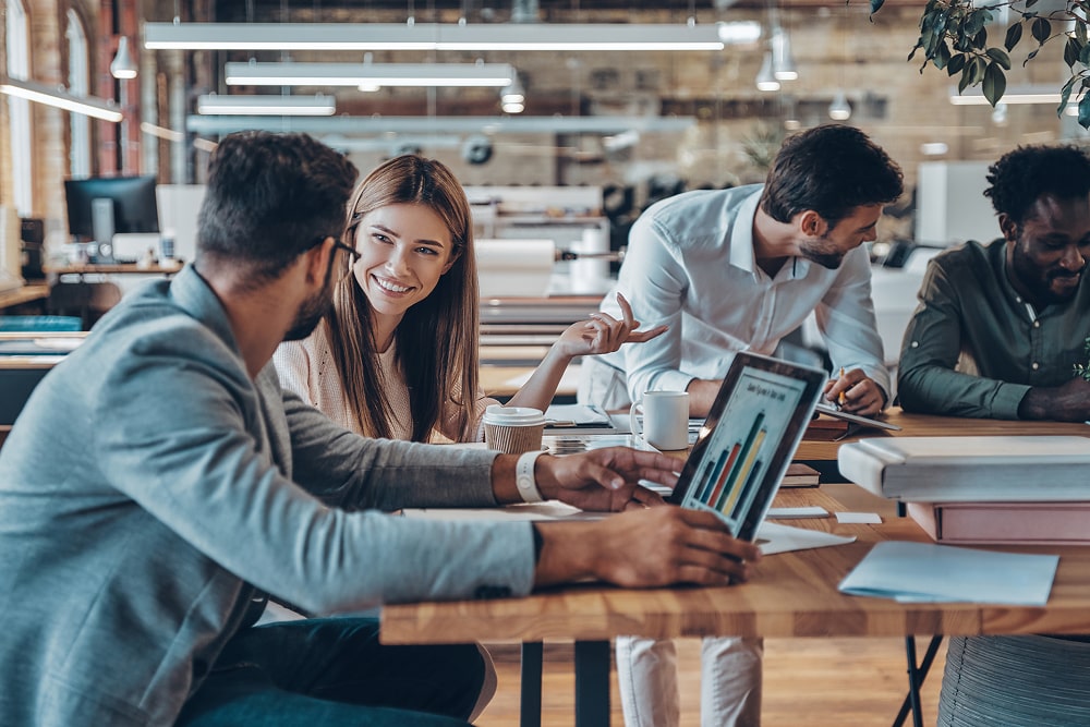 Group of young modern people in smart casual wear communicating and using modern technologies while working in the office